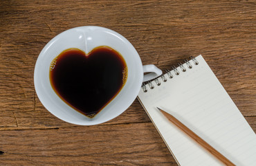 heart shape of black Coffee cup with notebook and pencil