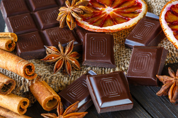 Dark chocolates with dry oranges, cinnamon and anise on burlap on rustic table