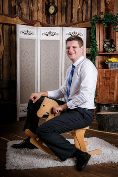 Happy Childish Young Man Is Riding On The Wooden Toy Horse. Adult Acting Like A Child Concept