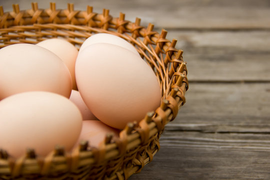 Chicken eggs on a wooden table in a wicker basket on the left.