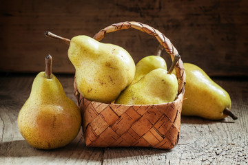 Ripe yellow pears in a wicker basket on an old wooden background