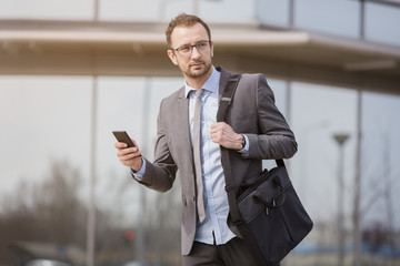 Businessman using smart phone in front of the blue glass business building   