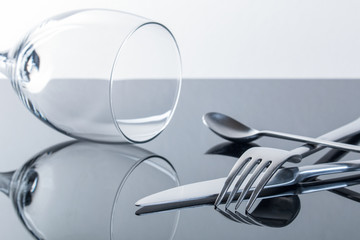 Messer, Gabel, Teelöffel und ein Weinglas auf glänzender, spiegelnder Tischplatte