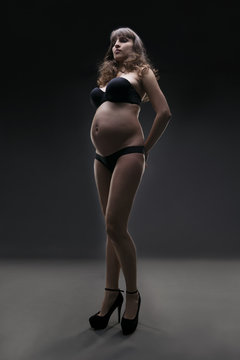 Young beauty and sexy caucasian pregnant woman in black lingerie on gray studio background