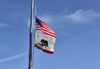 US and California flags at half mast on a rustic wood leaning flag pole.