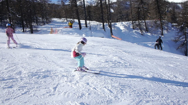 Young teenage girls follow their ski instructor showing giant slalom technique, down the slope in snake line. Sunny day and sun flare shows behind.
