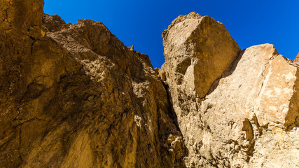 High sandstone cliffs painted in many glowing shades of orange, gold and red. Narrow canyon with vertical walls on both sides. Rocky landscape background. Golden canyon, Death Valley