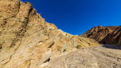 The gorge cuts into brightly colored sandstone rocks. Narrow canyon with vertical walls on both sides. Rocky landscape background. Sandstone formations in Golden canyon, Death Valley