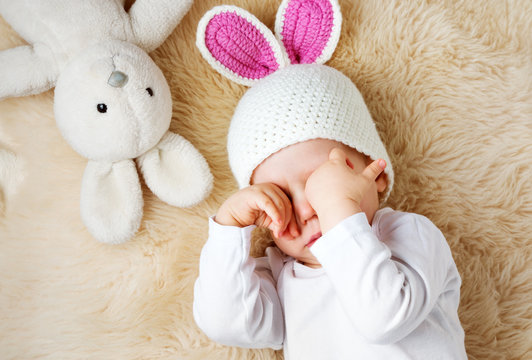 one year old baby lying in bunny hat on lamb wool