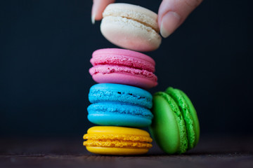 Colorful macaroons tower close-up on black background. Female hand takes one cookie
