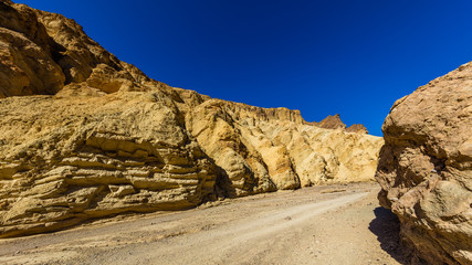 Fototapeta na wymiar High sandstone cliffs painted in many glowing shades of orange, gold and red. Narrow canyon with vertical walls on both sides. Rocky landscape background. Golden canyon, Death Valley