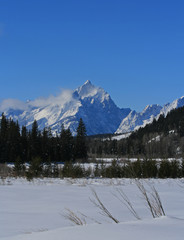 Snow mist blowing off Grand Tetons peaks  in front of snowfield