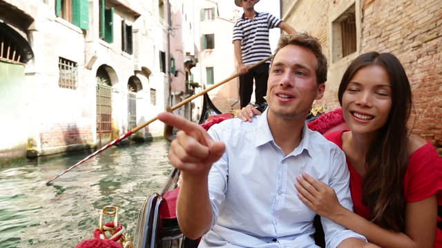 Romantic travel couple in Venice on Gondola ride romance in boat talking happy together on travel vacation holidays. Young multiracial couple sailing in venetian canal in gondole. Italy, Europe