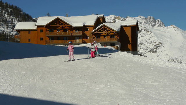 Young teenage girls take a slalom lesson, down the ski slope in snake line with background mountain range on sunny day.
