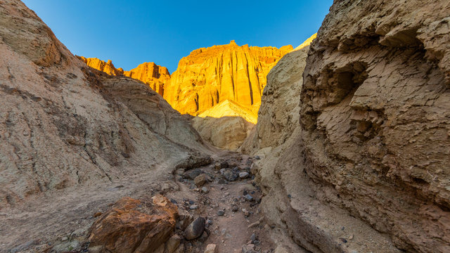 The gorge cuts into brightly colored sandstone rocks. Narrow canyon with vertical walls on both sides. Rocky landscape background. Sandstone formations in Golden canyon, Death Valley