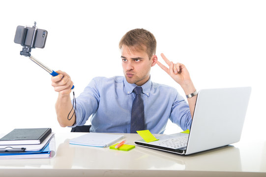  businessman in shirt and tie sitting at office computer desk holding selfie stick shooting self portrait photo