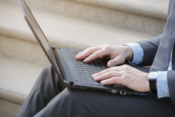 Close up of male hands typing on laptop keyboard outdoors 