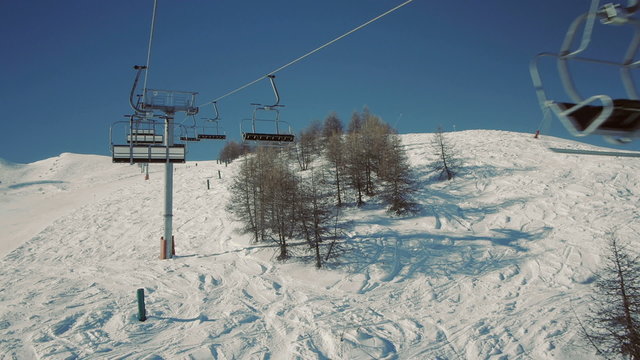 Riding a chair lift in first person view above the ski slope on sunny winter day.
