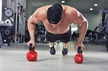 Handsome powerful athletic man performing push ups with kettle bell. Strong bodybuilder with  perfect shoulders, biceps and triceps.