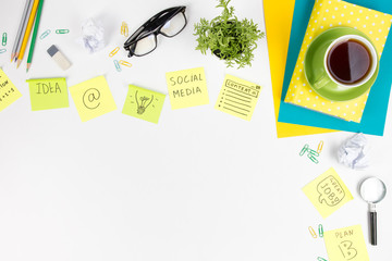 Office table desk with green supplies, blank note pad, cup, pen, glasses, crumpled paper, magnifying glass, flower on white background. Top view