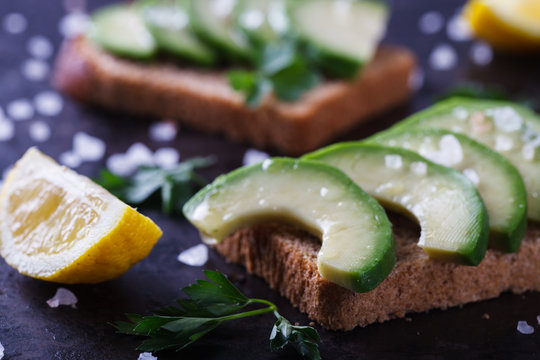 Toast with avocado on rye bread with parsley and salt on a dark background.