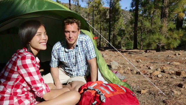 Camping couple in tent taking smartphone selfie self portrait photo picture. Campers smiling happy outdoors in forest. Happy people having fun in outdoor activity. Asian woman, Caucasian man.