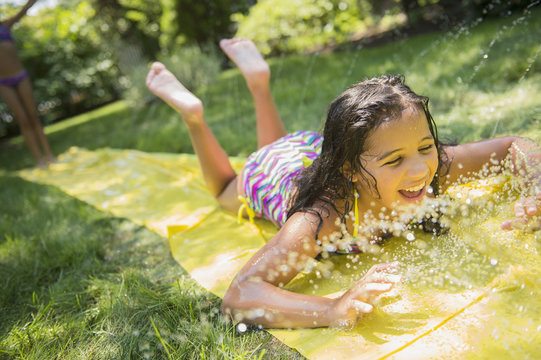 Girl playing on water slide in backyard