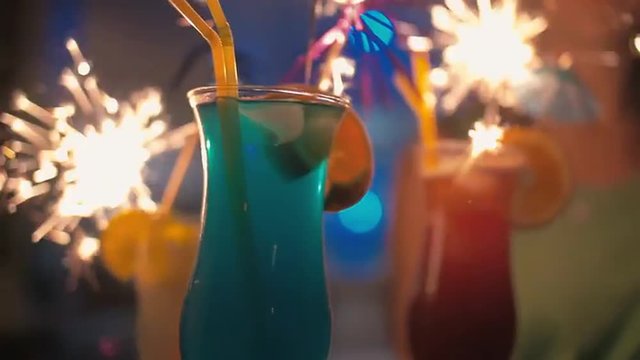 Slow motion steadicam and close-up shot of colorful summer cocktails with sparklers on tray held by young woman