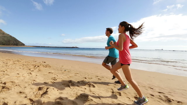 People running on beach training and jogging. Runners couple working out exercising together. Asian woman model and fit Caucasian fitness runner man.