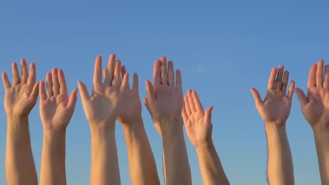 Slow motion of many hands raised against blue sky background.  Volunteering or voting concept