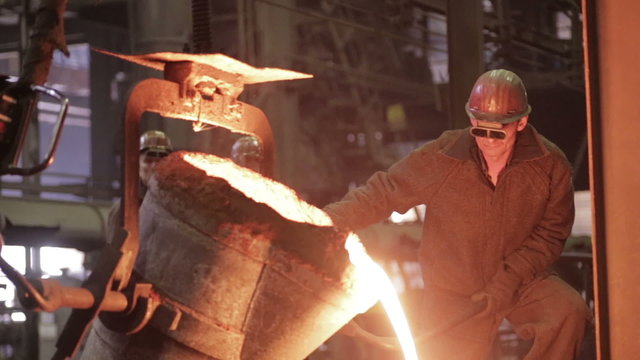 Worker on steel plant operates with molten metal. HD.