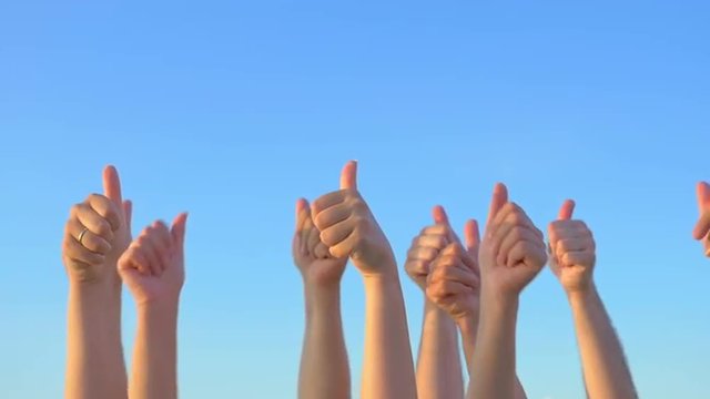 Slow motion of raising many hands with thumbs-up on blue sky background. Approval, praising and support