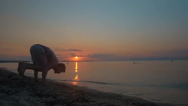 Slow motion of a young man doing handstand and walking on hands on the beach at sunset. Performing acrobatic skills
