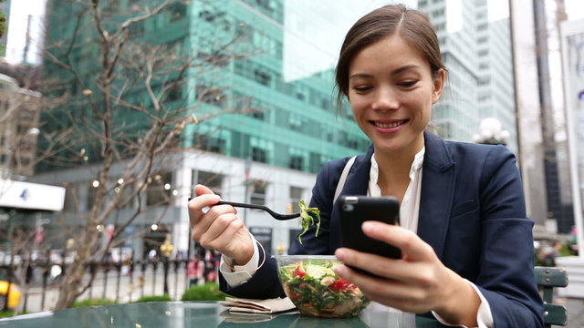 Young business woman eating salad on lunch break in City Park living healthy lifestyle working on smart phone. Happy smiling multiracial young businesswoman, Bryant Park, Manhattan, New York City, USA