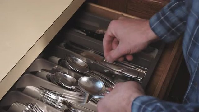 a person opens a silverware cabinet drawer and grabs silverware. Then person puts away silverware utensils.