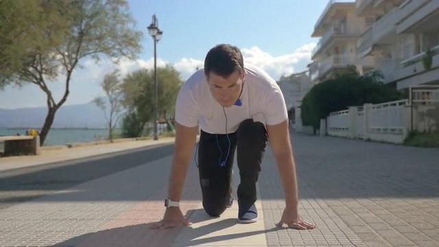 Slow motion steadicam shot of a young man taking a run from crouch start and jogging along the seafront. Everyday workout to keep fit