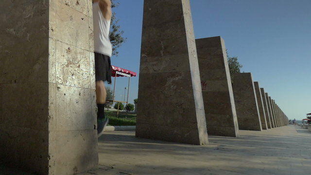 Slow motion steadicam shot of a teenager making somersault in jump between the stone columns on the sea front. Extreme sport