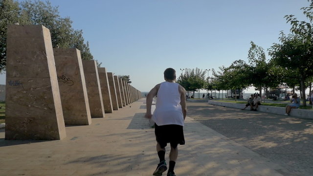 Slow motion steadicam shot of a young sportsman showing parkour skills. He sliding on stone bench and doing somersault