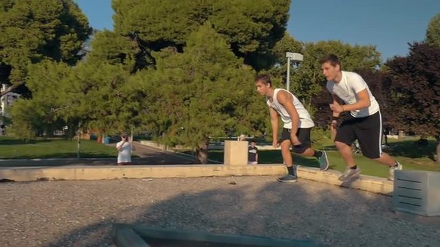 Slow motion steadicam shot of two men doing parkour in the city park.  Young people having risky and extreme sportive hobby