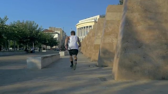 Slow motion steadicam shot of a young sportsman performing extreme running in the city with somersaults and tumblesets
