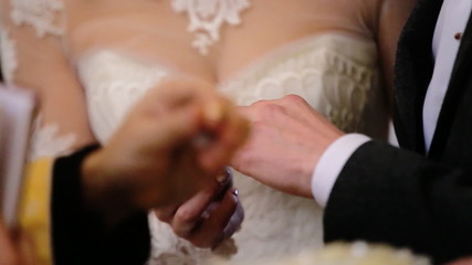 Lovely beautiful  bride wearing fashionable white wedding dress  put gold ring on a finger of a young groom in  black suit.