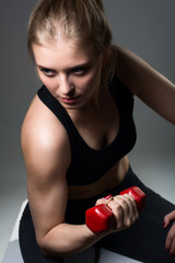 Athletic young woman doing a fitness workout with dumbbells on grey studio background