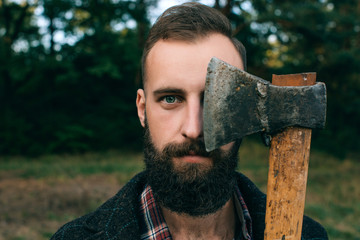 Portrait brutal bearded and moustached woodcutter hipster Gypsy man in the forest with ax