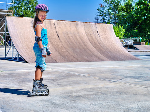 Girl wearing protection riding on roller skates in skatepark.