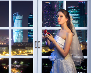 Gorgeous girl bride at a window. Outside the window the night. The night city, skyscrapers. Girl in...