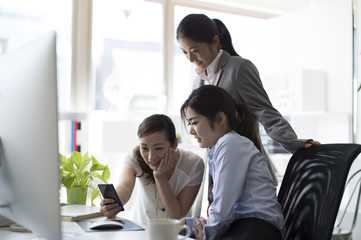 Three women are looking at the screen of a smart phone together