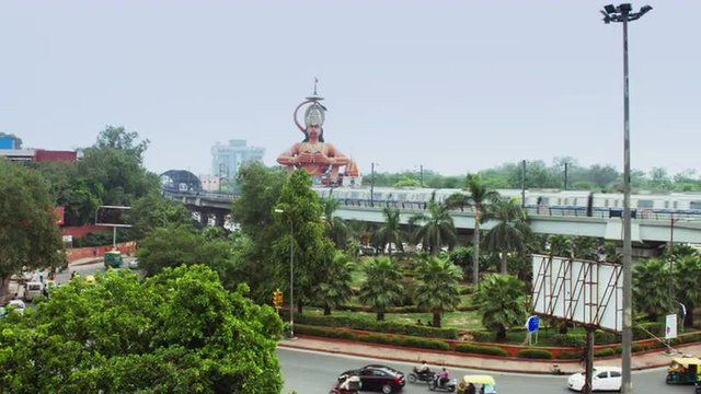 Locked-on shot of metro train moving in front of giant statue of Lord Hanuman, Karol Bagh, New Delhi, India 