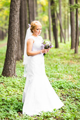 Fototapeta na wymiar Young bride in wedding dress holding bouquet, outdoors