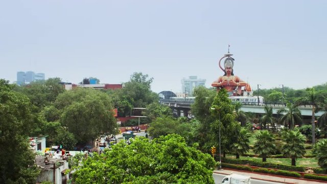 Locked-on shot of metro train moving in front of giant statue of Lord Hanuman, Karol Bagh, New Delhi, India 