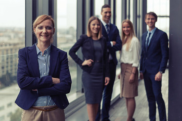 Corporate portrait of young business woman with her colleagues in background. Post processed with vintage film and sun filter.